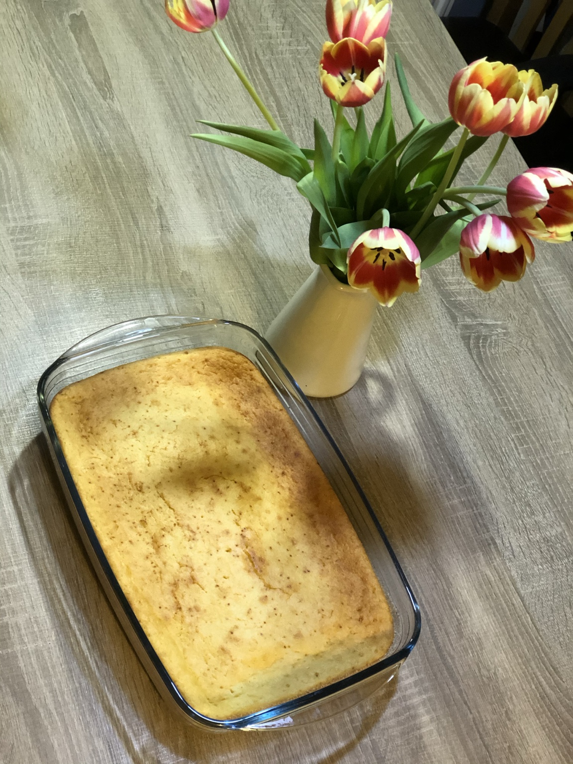 Mălai dulce copt în tavă de sticlă, pe masa din lemn, lângă o vază cu lalele